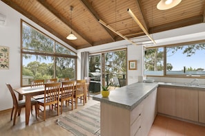 A modern kitchen with large windows, wooden ceiling beams, and a dining area with a table and chairs. - Ocean's Course (Lorne)