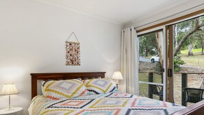 A bedroom with a bed, a bedside lamp, a hanging decoration, and a view through a glass door. - Ocean's Course (Lorne)