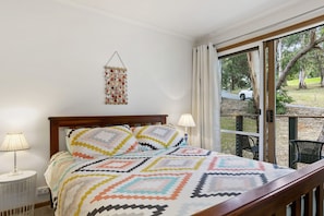 A bedroom with a bed, a bedside lamp, a hanging decoration, and a view through a glass door.