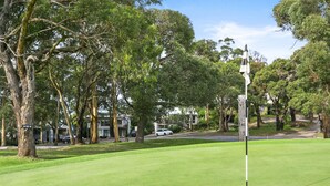 A golf course with a flagstick, trees, and a residential area in the background. - Ocean's Course (Lorne)