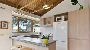 A modern kitchen with a central island, bar stools, a microwave, and a refrigerator. - Ocean's Course (Lorne)