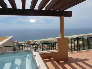 Enjoy breathtaking ocean views from this balcony featuring a hot tub and a covered pergola.