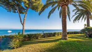 A coastal landscape with palm trees, a grassy area, and a view of the sea with a boat in the distance. - SUN OF ALCANADA - Apartment with sea views in Alcanada. Free WiFi (Alcúdia)
