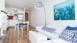 A modern living room with a white sofa, blue patterned pillows, and a cityscape painting on the wall. - SUN OF ALCANADA - Apartment with sea views in Alcanada. Free WiFi (Alcúdia)