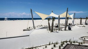A beachside promenade with a clear view of the ocean, a lifeguard tower, and a few palm trees.