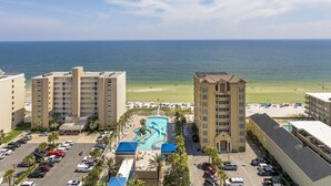 A hotel with a pool, beach view, and parking lot.