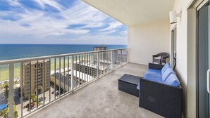 A balcony with a view of the ocean, a wicker sofa, and a chair.