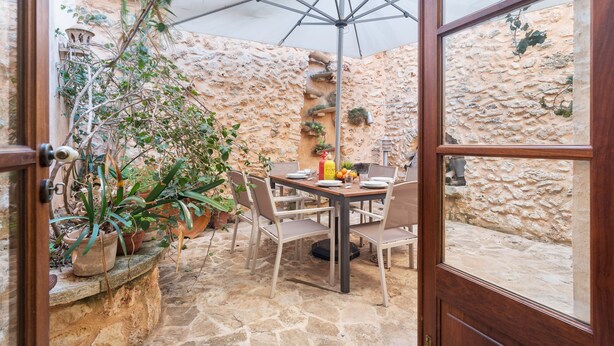 A stone-walled patio with a wooden table and chairs, potted plants, and a large umbrella. - CAN VALLORI - Nice house with interior terrace in Sencelles. Free WiFi (Sencelles)