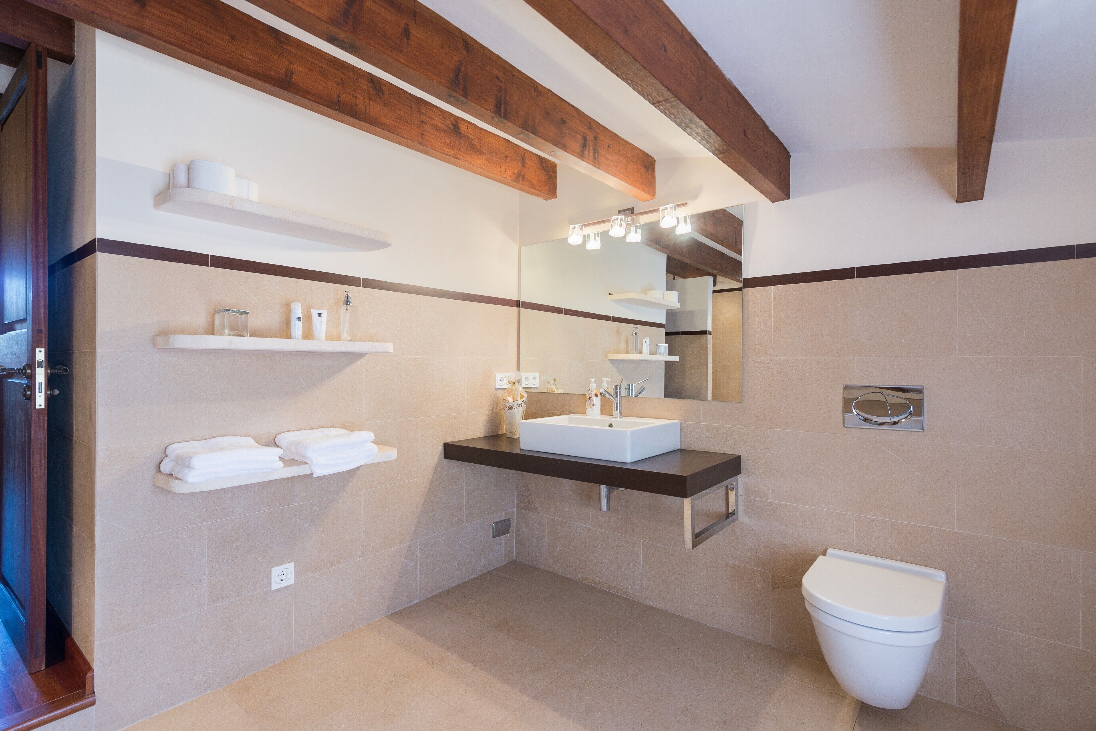 Ein modernes Badezimmer mit einem großen Spiegel, einem weißen Waschbecken und einer Toilette.