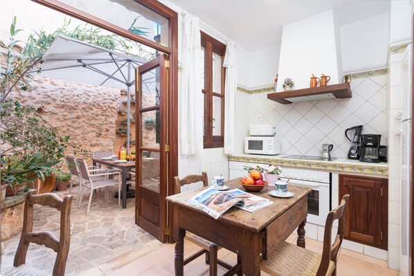 Une cuisine avec une table en bois, des chaises, un four à micro-ondes, une machine à café et une fenêtre donnant sur un jardin.