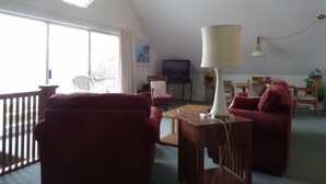 A living room with a sloped ceiling, a large window, a television, and red furniture. - Oceanfront Carriage House Apt. w/ Spectacular Views (York)