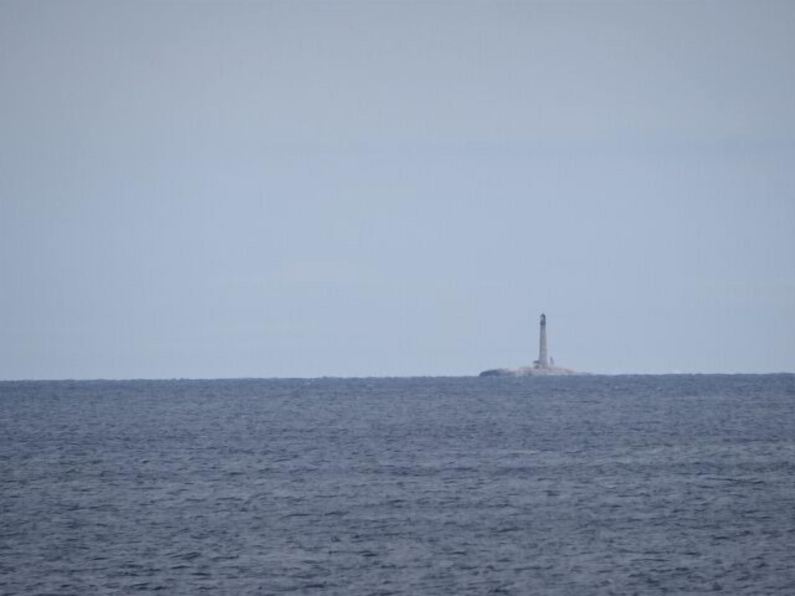 Ein Leuchtturm auf einer kleinen Insel inmitten ruhiger See.