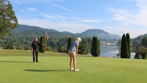 A golf course with a flagstick and a golfer in the foreground, surrounded by trees and a lake in the background. - Starstorm Mountain Apartment
Lakeview deck & hiking trail, near many activities. (Lake Junaluska)