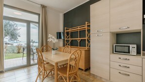 A modern kitchen with a dining table, chairs, a microwave, and a view of the outdoors. - Villenpark Sanghen - Two-Room Apartment in Casa Centrale (Villaggio Sanghen)