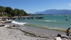 A beach with a rocky shoreline, a pier, and boats in the water. - Villenpark Sanghen - Two-Room Apartment in Casa Centrale (Villaggio Sanghen)