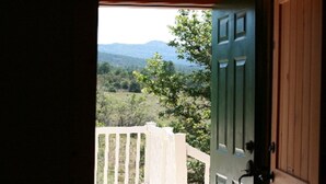 Uitzicht vanuit een kamer met een houten deur naar een balkon. Het balkon kijkt uit over een bergachtig landschap met bomen en een houten hek.