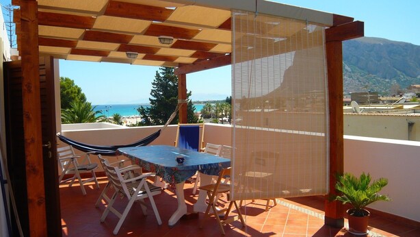 A covered outdoor seating area with a table and chairs, a hammock, and a potted plant.