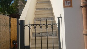 A staircase with a metal gate leading to a door, a number '18' sign on the wall, and a clear blue sky in the background.