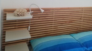 A bedroom with a wooden slatted headboard, a bedside table with a lamp, and a bed with blue-striped pillows.