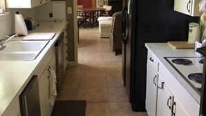 A narrow kitchen with a refrigerator, stove, and sink. There is a dining area in the background with a table and chairs. - Patterson Place is cozy and has Beautiful Waterfront (McQueeney)
