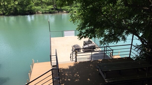 A wooden dock extending into a calm lake, with a grassy area and a bench. - Patterson Place is cozy and has Beautiful Waterfront (McQueeney)