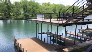 A wooden dock extending into a calm body of water, with a metal staircase leading up to a covered area. - Patterson Place is cozy and has Beautiful Waterfront (McQueeney)