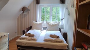 Ein Schlafzimmer mit Schlafgalerie, einem Bett mit weißen Leinen, zwei Kissen, einer Nachttischlampe und einer Holzkommode.