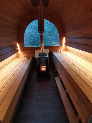 Un sauna avec des bancs en bois, un système de chauffage central et une vue sur les arbres à travers une fenêtre semi-circulaire.