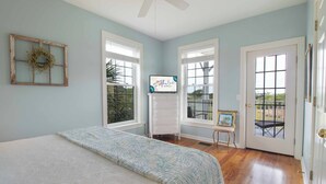Un dormitorio con cama, cómoda, televisor y puerta que da a un balcón.