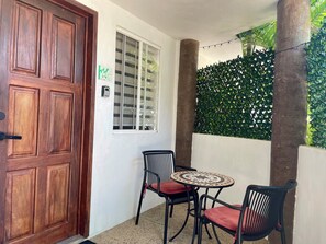 A wooden door, a window with a frosted glass panel, a small round table with chairs, and a green leafy wall.