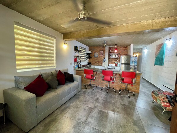 A modern kitchen with a bar area, a grey sofa with red cushions, and a skateboard.