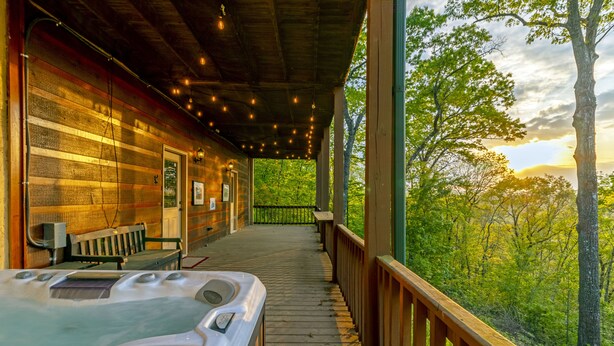 En træhytte med jacuzzi på verandaen, en bænk og udsigt til skoven.