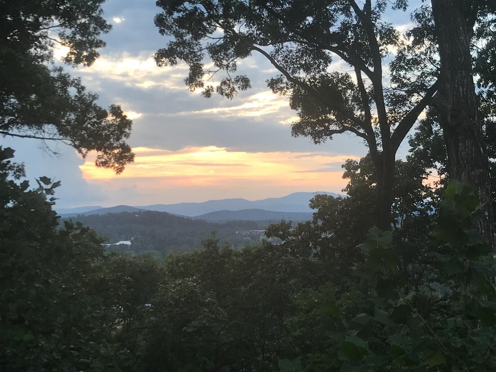 A view of a mountainous landscape with trees and a sunset.