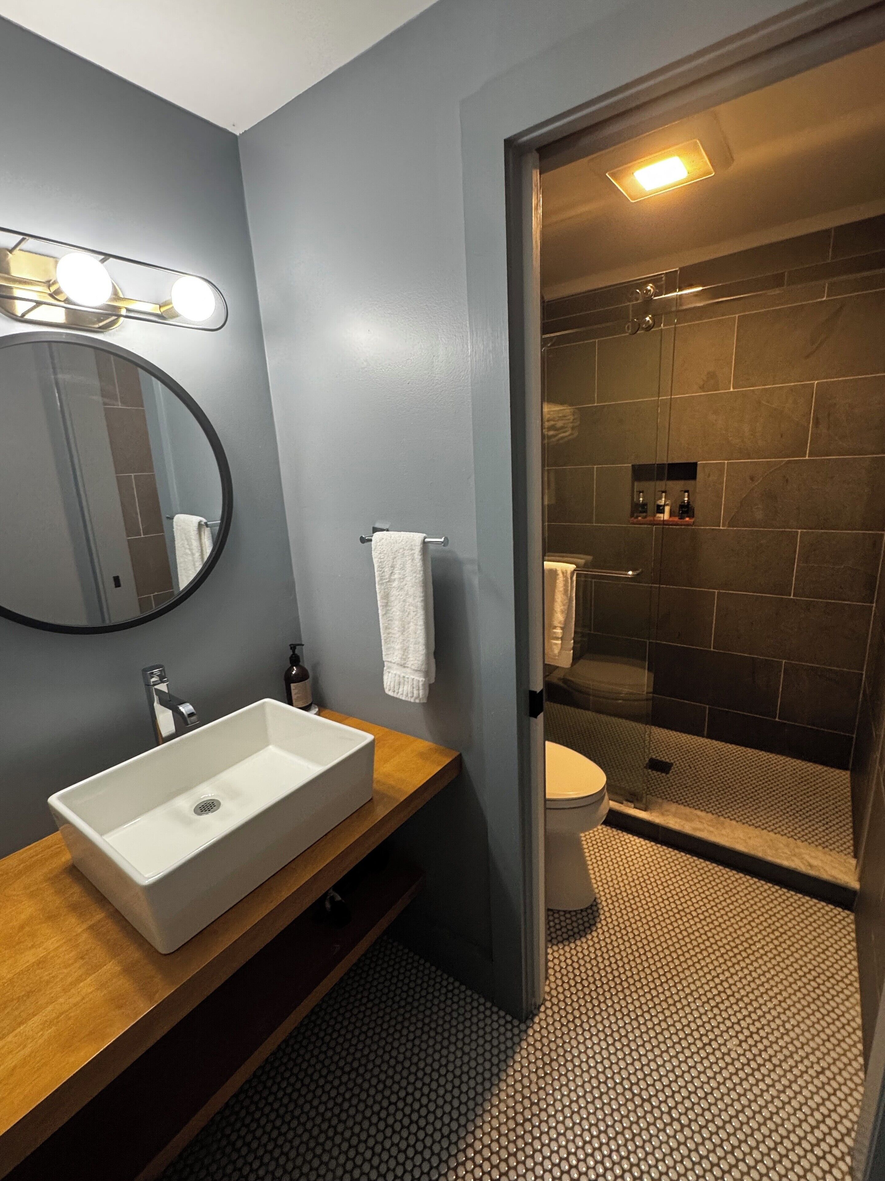 A modern bathroom with a rectangular sink, a round mirror, and a shower area with a glass door.