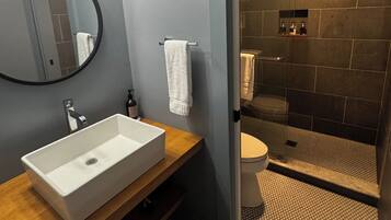 Un baño moderno con un lavabo rectangular, un espejo redondo y una zona de ducha con puerta de cristal.