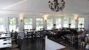 A restaurant with multiple dining tables and chairs, a bar area with a counter, and a chandelier. - Shelter Harbor Inn (Westerly)
