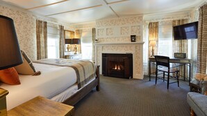 A hotel room with a large bed, a fireplace, a desk with a chair, and a television. - Shelter Harbor Inn (Westerly)