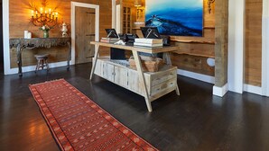 A room with a wooden floor, a red patterned rug, a wooden desk with books and a laptop, a large painting on the wall, and a chandelier. - Shelter Harbor Inn (Westerly)