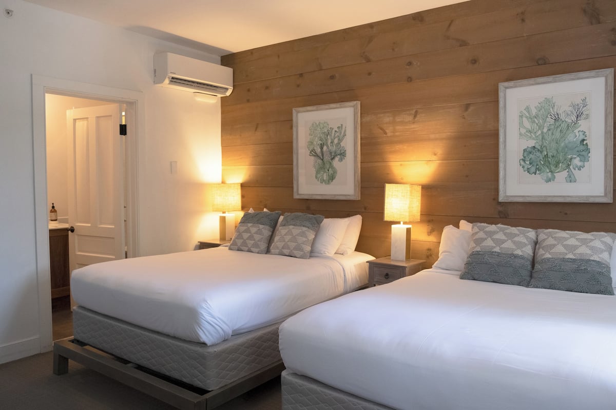 Hotellihuone, jossa on kaksi sänkyä, seinissä puupanelointi ja kehystettyjä kasvitieteellisiä taideteoksia.