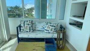Ein Zimmer mit einer Couch, einem Holztisch und einem Fenster mit Blick auf Gebäude und Bäume.
