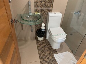 Une salle de bain avec un lavabo en verre, des toilettes et un espace douche.