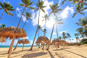 A beach with palm trees and thatched umbrellas. - Los Corales Beach Village - Your private paradise - 2BR first floor - LT#A2 (Bávaro)