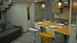 A modern kitchen with a dining table set for four, a sofa, and a yellow stool. - VILLA ROSA - Apartment n. 2 "GIGLIO" (4 beds): (Napoli)