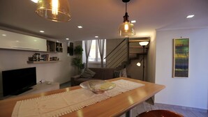 A modern living room with a wooden dining table, a TV, and a staircase leading to another level. - VILLA ROSA - Apartment n. 2 "GIGLIO" (4 beds): (Napoli)