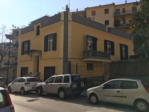 A two-story building with a yellow facade, black shutters, and a balcony.
