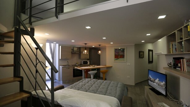 A modern bedroom with a bed, a desk, and a TV. There is a staircase leading to an upper level. - VILLA ROSA - Apartment n. 2 "GIGLIO" (4 beds): (Napoli)