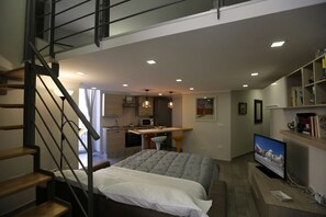 A modern bedroom with a bed, a desk, and a TV. There is a staircase leading to an upper level. - VILLA ROSA - Apartment n. 2 "GIGLIO" (4 beds): (Napoli)