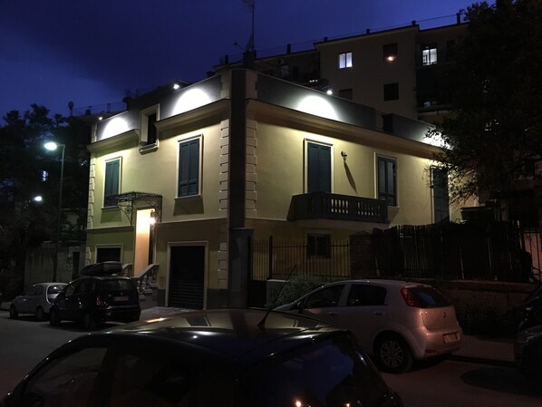 A two-story building with a balcony, a gated entrance, and parked cars in front.