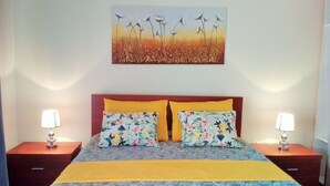 Een slaapkamer met een bed, twee nachtkastjes, twee lampen en een wanddecoratie.