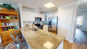 A kitchen with white cabinets, a granite countertop, a stainless steel refrigerator, and a microwave. - Spacious w/ Fantastic Views, Large Balcony, Walkable Location! (Tybee Island)